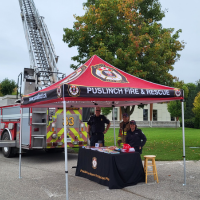 A photograph of three volunteer firefighters under a public education tent. 